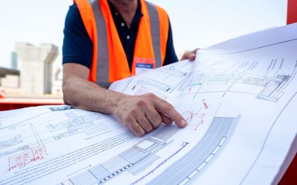Engineer reviewing architectural blueprints outdoors.